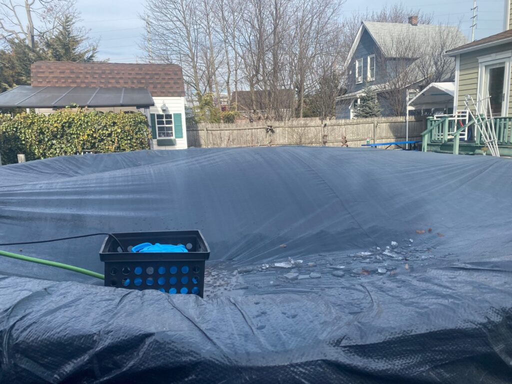Automatic cover pump in a milk crate on a solid winter pool cover with a hose running off the cover
