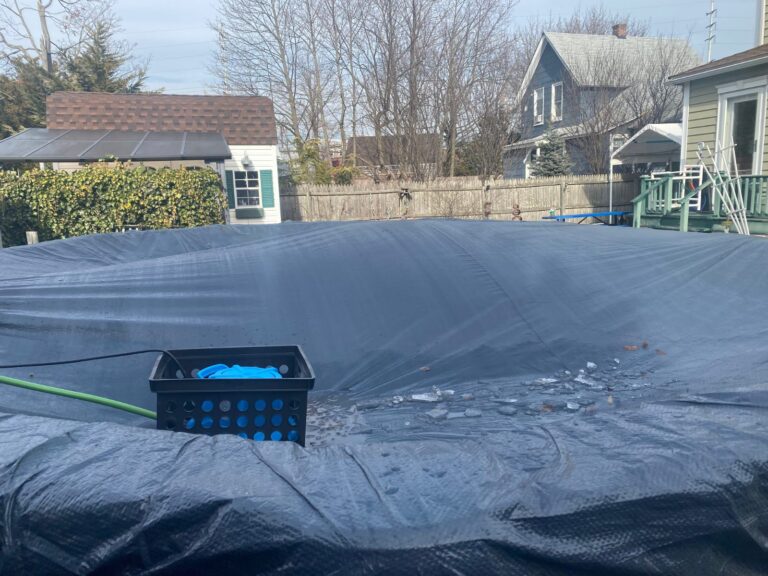 Automatic cover pump in a milk crate on a solid winter pool cover with a hose running off the cover
