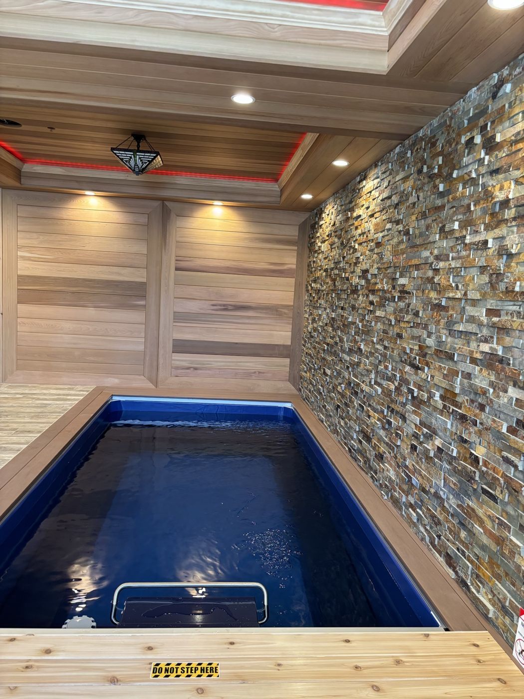 A finished indoor swim spa with cedar walls and a stone accent wall
