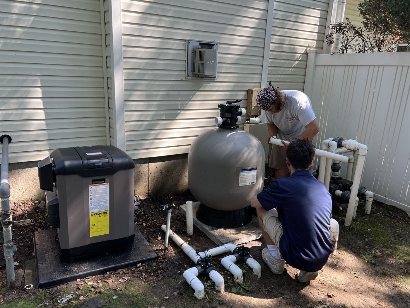 Two techs plumbing in a new pool heater and filter