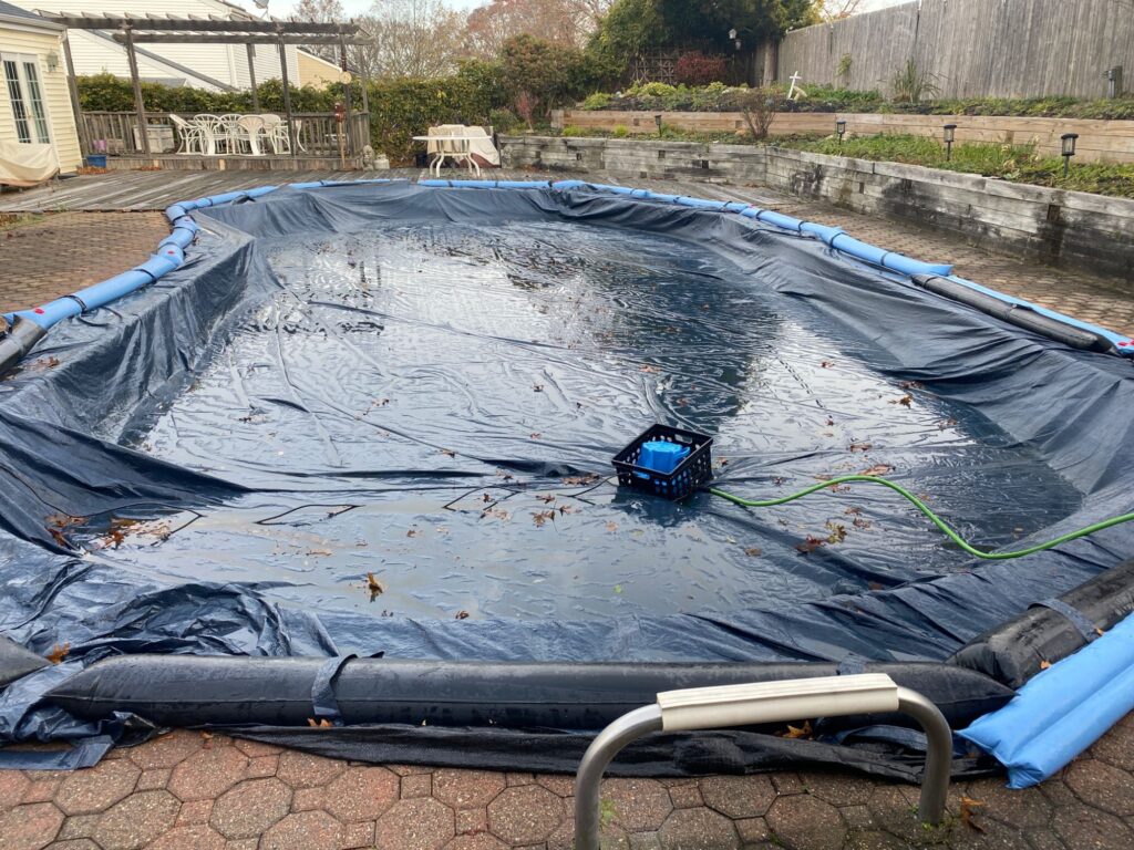 Cover pump running on a solid winter pool cover with water bags around the edge