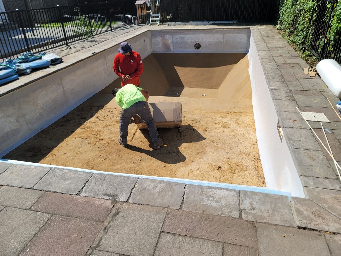 Two techs setting the floor of an empty pool before a new liner